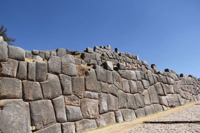 Low angle view of a stone wall against clear blue sky