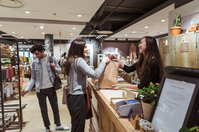 Smiling saleswoman giving merchandise to customer at checkout counter