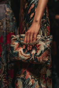 Female hands holding a small colorful designer handbag with a pattern and a silver chain. 
