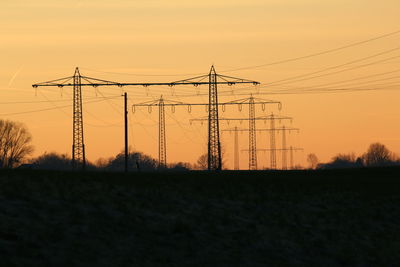 Silhouette electricity pylons on field against sky during sunset