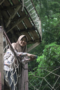 Woman standing by fence against tree