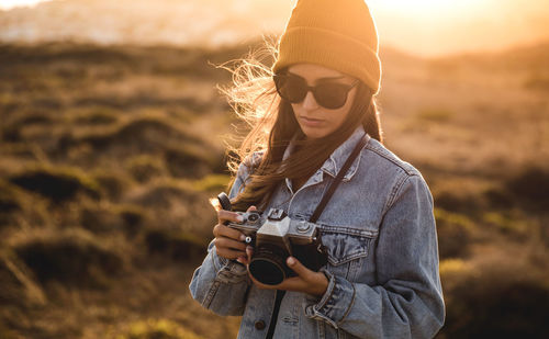 Young woman holding camera while standing on land