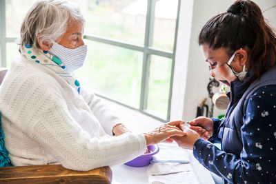 Woman wearing mask doing manicure of customer at home