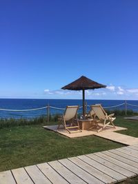 Lounge chairs by swimming pool at beach against blue sky