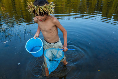 Full length of shirtless boy holding water in lake