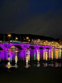 Illuminated city by lake against sky at night