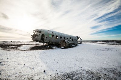 Abandoned airplane crash on snowy field against sky during sunset