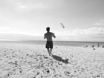Rear view of man playing with kite on shore against sky