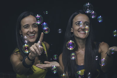 Happy friends blowing bubbles against black background