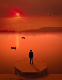 Rear view of man standing by lake during sunset