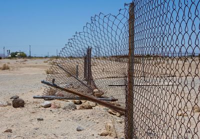 Damaged chainlink fence on field against clear sky