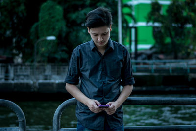 Side view of young man using phone on railing