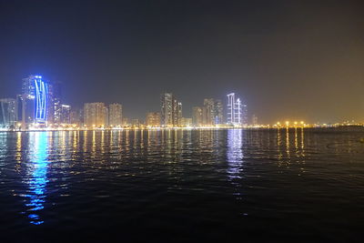 Illuminated city by river against sky at night