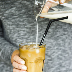 Close-up of hand holding pouring milk in cold coffee on table