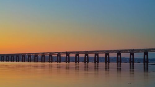 Pier over sea against orange sky