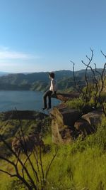 Full length of young woman sitting on rock against sky