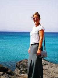 Portrait of smiling young woman standing on beach against clear sky