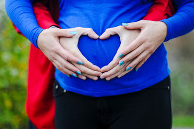 Midsection of pregnant woman with husband making heart shape on abdomen