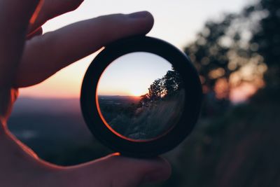 Close-up of hand holding mirror against sunset sky