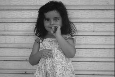 Portrait of cute girl holding small box while standing against wall