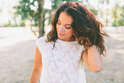 Close-up of woman with hand in hair against trees during day