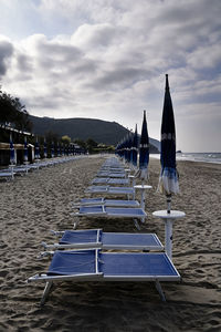 Deck chairs on beach against sky