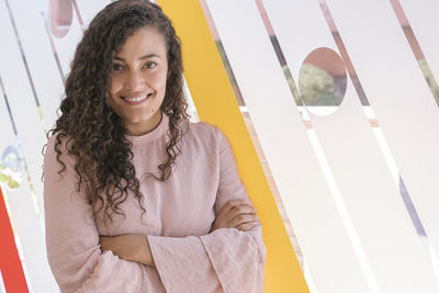 Portrait of smiling young woman with arms crossed standing in office