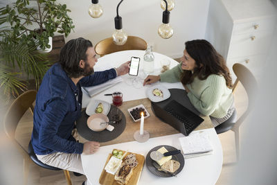 High angle view of heterosexual couple discussing over smart phone at table