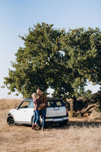 Man with woman standing by tree against sky