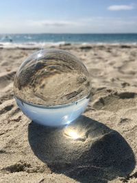 Close-up of crystal ball on sand at beach against sky