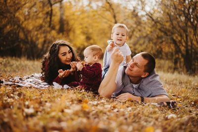 Happy siblings and son on tree during autumn
