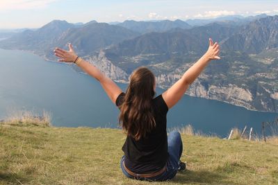 Rear view of woman with arms raised sitting on mountain