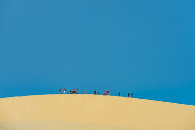 Low angle view of people on sand dune at desert against clear blue sky