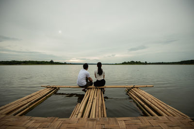 Couple sitting on wooden raft in lake against sky
