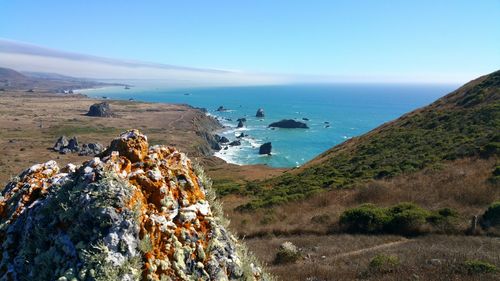 Cliff's edge with rusty colored rock overlooking foggy ocean vista.