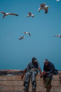 People with birds flying against sky