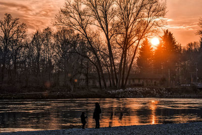 Silhouette mother with son standing at lakeshore against sky during winter