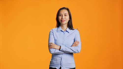 Portrait of young woman standing against yellow background