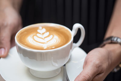 Close-up of hand holding cappuccino served on table