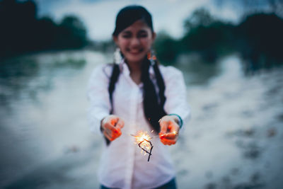 Smiling young woman holding umbrella while standing in water