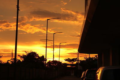 Street by silhouette trees against orange sky