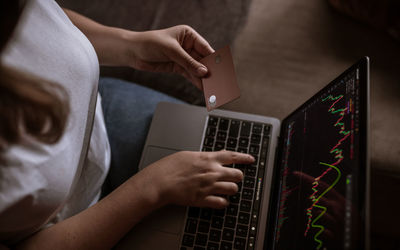 Young woman looking at the market on laptop with card on hand