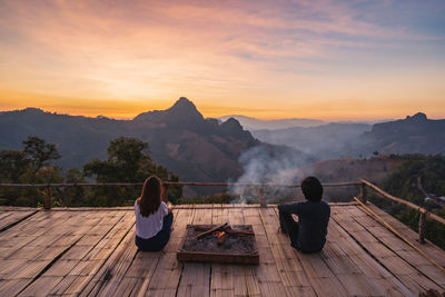 Rear view of men sitting on wood against sky during sunset