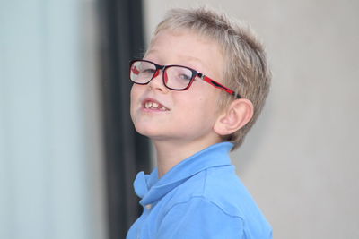 Side view of cute boy wearing eyeglasses looking away while standing against wall
