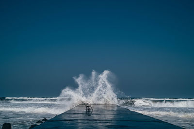 Waves splashing on sea against clear blue sky