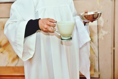 Midsection of priest holding vessel of bptism