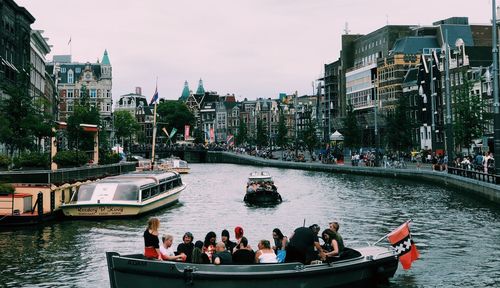 People on boats in river by cityscape against sky