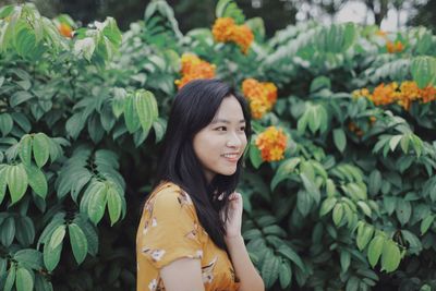 Smiling young woman standing against plants