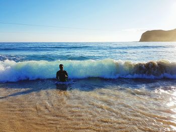 Man sitting on beach against clear sky