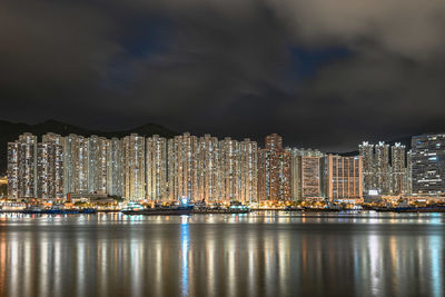 Illuminated city by sea against sky at night